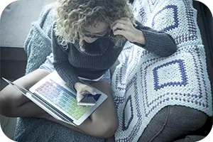 Woman sitting on her couch looking over plan options on her laptop.